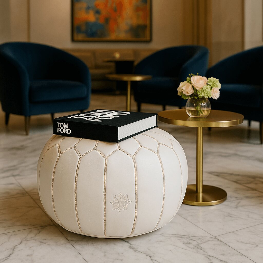 White leather pouf styled in a modern lounge with a book and golden side tables