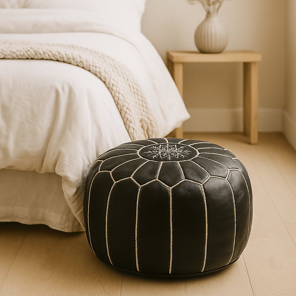 Black Moroccan leather pouf at the foot of a bed in a warm-toned minimalist bedroom