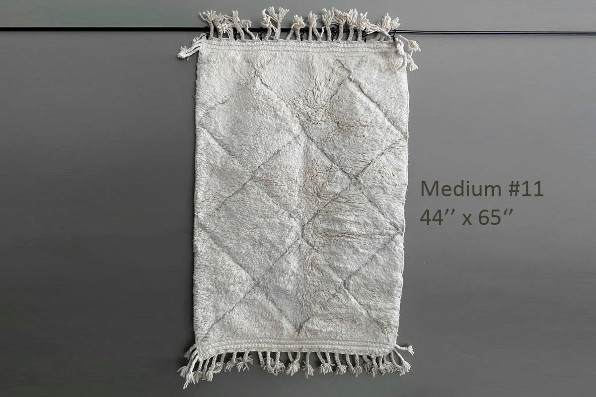 Cream-colored wool rug with diamond pattern and knotted fringe edges, 44" x 65".