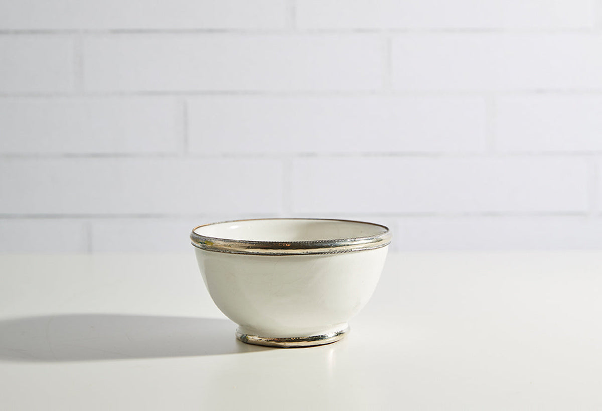 Cream-colored glazed ceramic bowl with silver-tone metallic trim on rim and base.