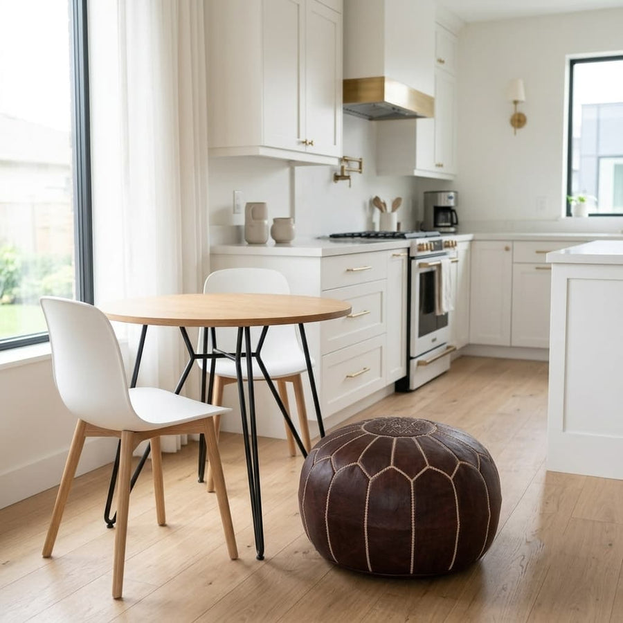 Dark brown leather pouf used as extra seating beside a round dining table in a bright white kitchen
