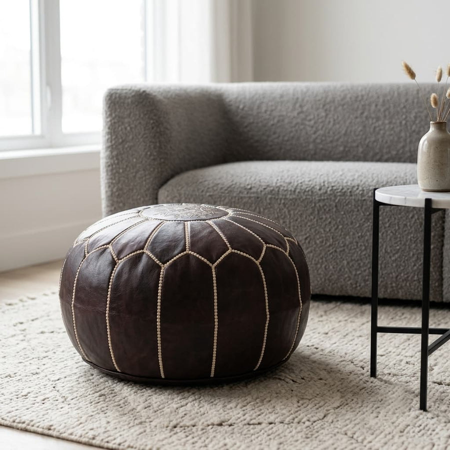 Dark brown Moroccan leather pouf on a textured cream rug in front of a grey boucle sofa