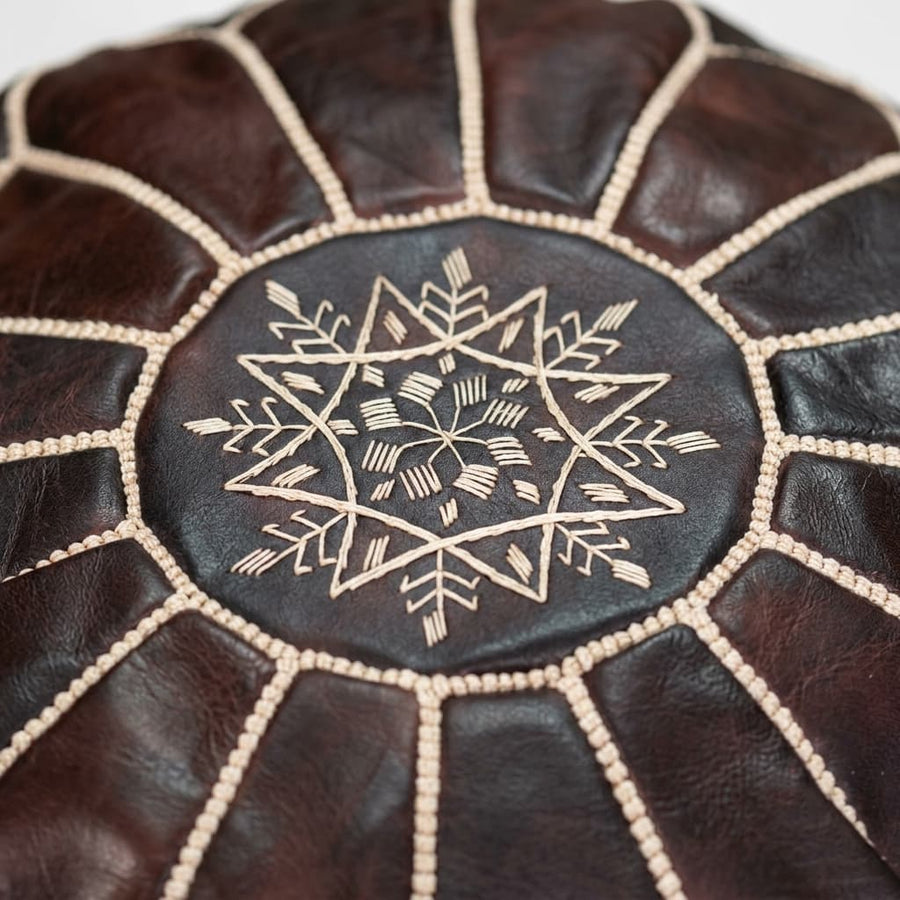Close-up of the hand-embroidered beige eight-pointed star and whipstitch seams on the dark brown leather pouf top panel