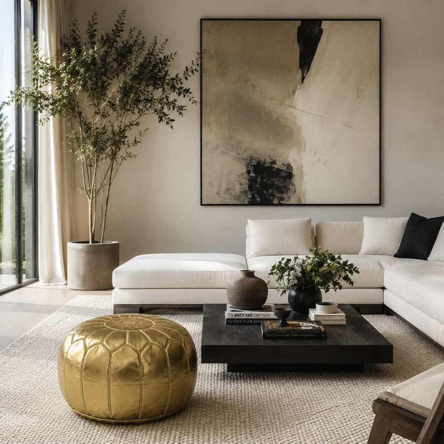 Gold leather pouf beside a low black coffee table in a bright modern living room with a white sofa