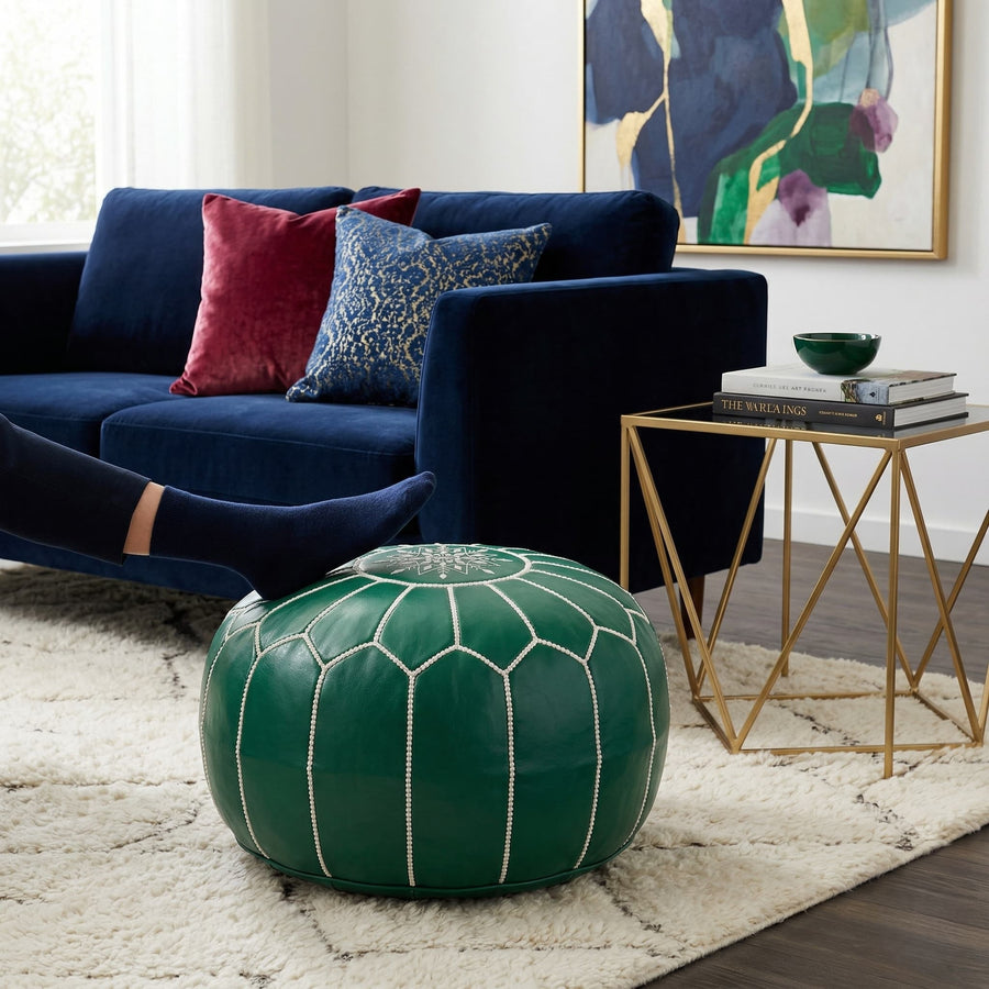 Green leather pouf used as a footrest on a cream shag rug beside a navy velvet sofa and gold side table