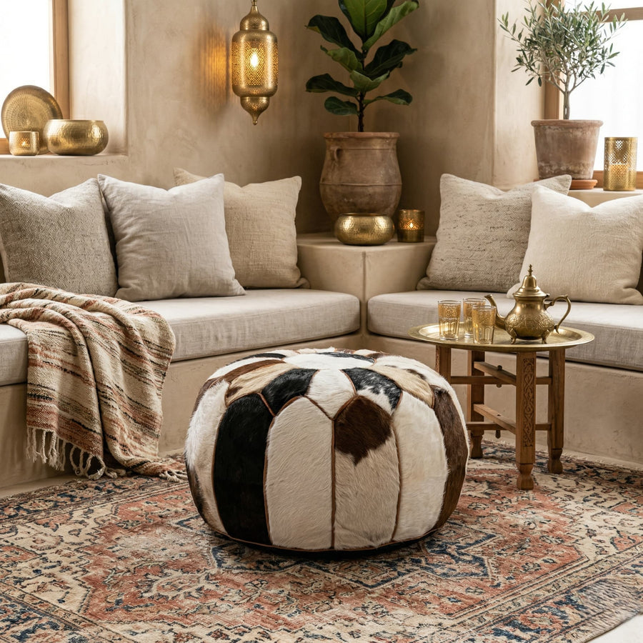 Cowhide patchwork pouf styled in a Moroccan riad lounge with linen seating, a brass tea tray and a vintage rug