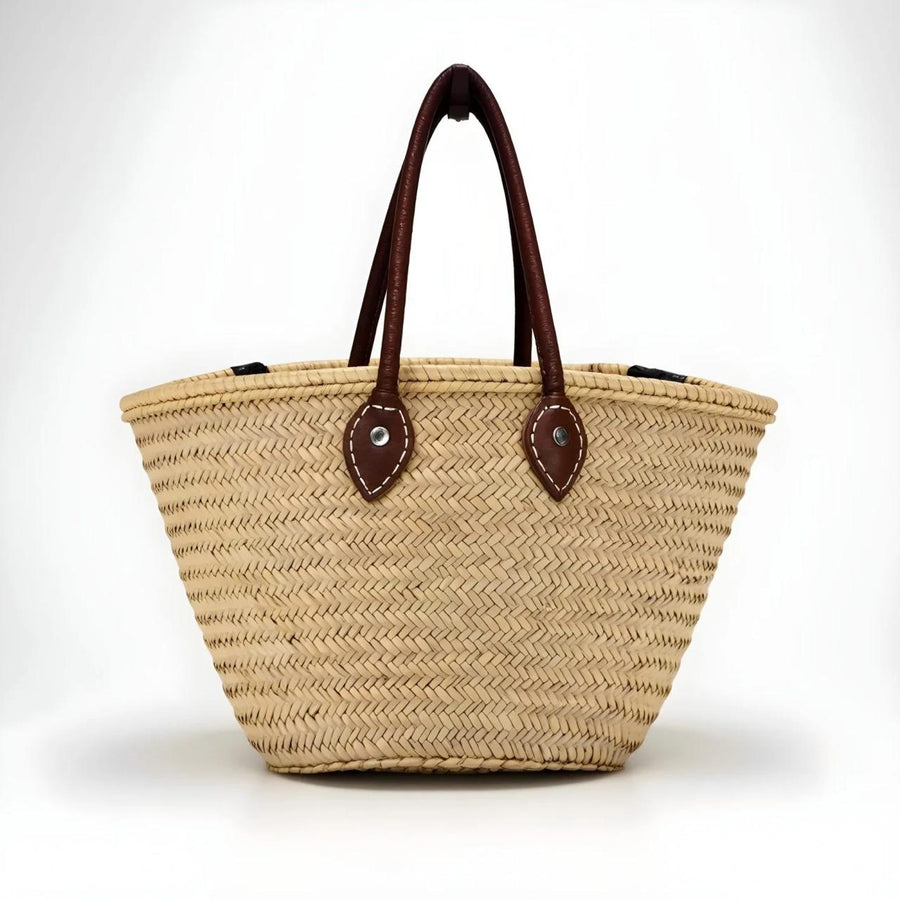 Handwoven Moroccan palm leaf basket tote with long dark brown leather handles, front view on a plain white background