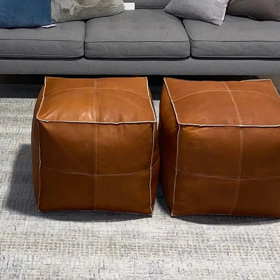 Pair of brown square leather pouf ottomans used as footstools in front of a sofa