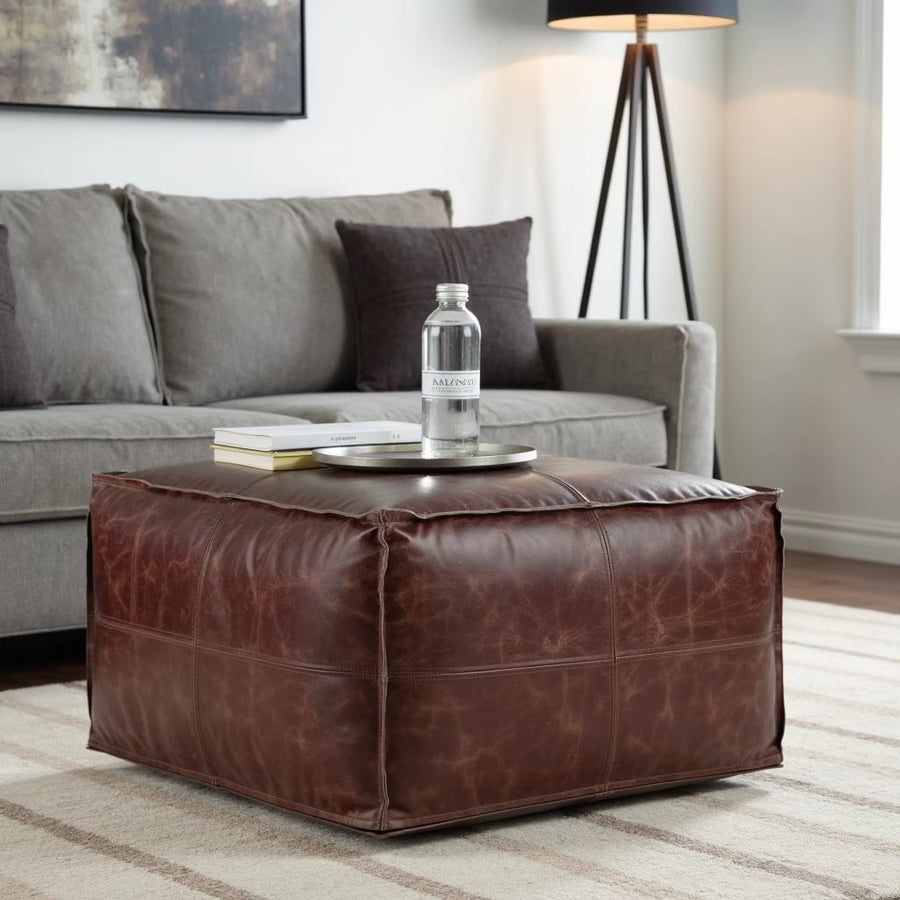 Dark brown square leather pouf beside a grey sofa with a floor lamp