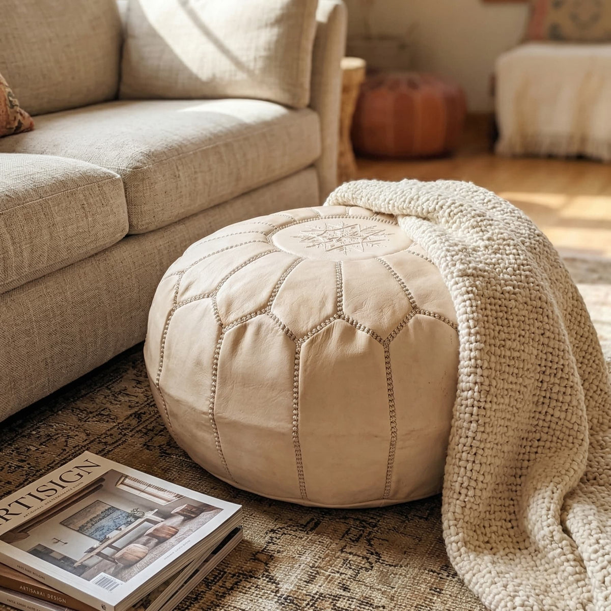 Cream undyed leather pouf beside a sofa with a draped throw