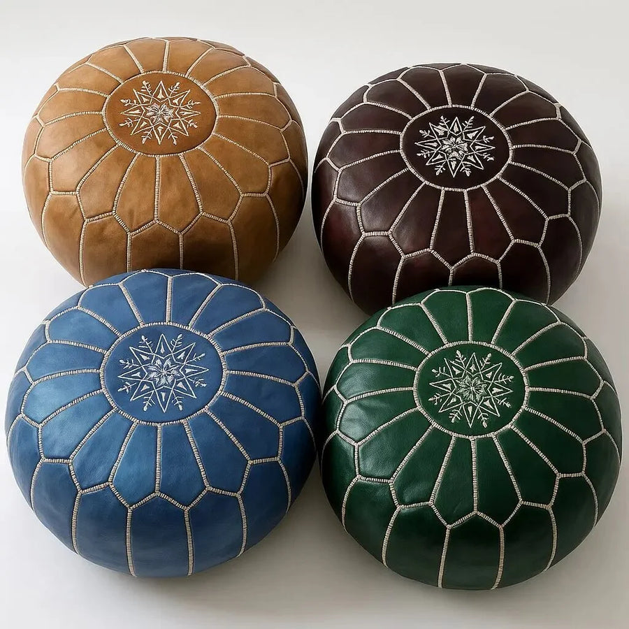 Set of four Moroccan round leather poufs in camel tan, dark brown, cobalt blue and emerald green, hand-embroidered star medallions, on a white studio background