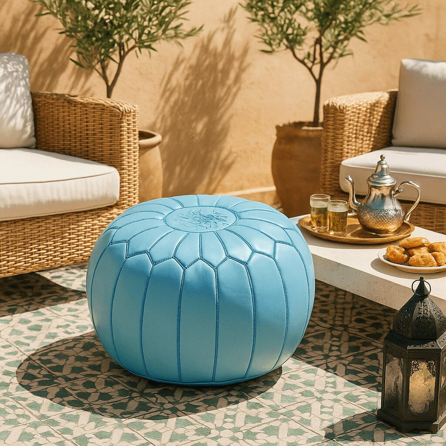 Sky blue Moroccan pouf on a tiled patio with rattan chairs, olive trees and a brass Moroccan tea set