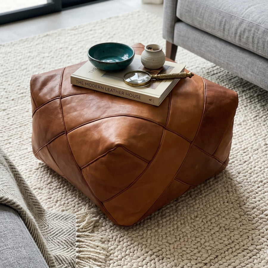 Close-up of the diamond-stitched square pouf holding a book, ceramic bowl and brass magnifier