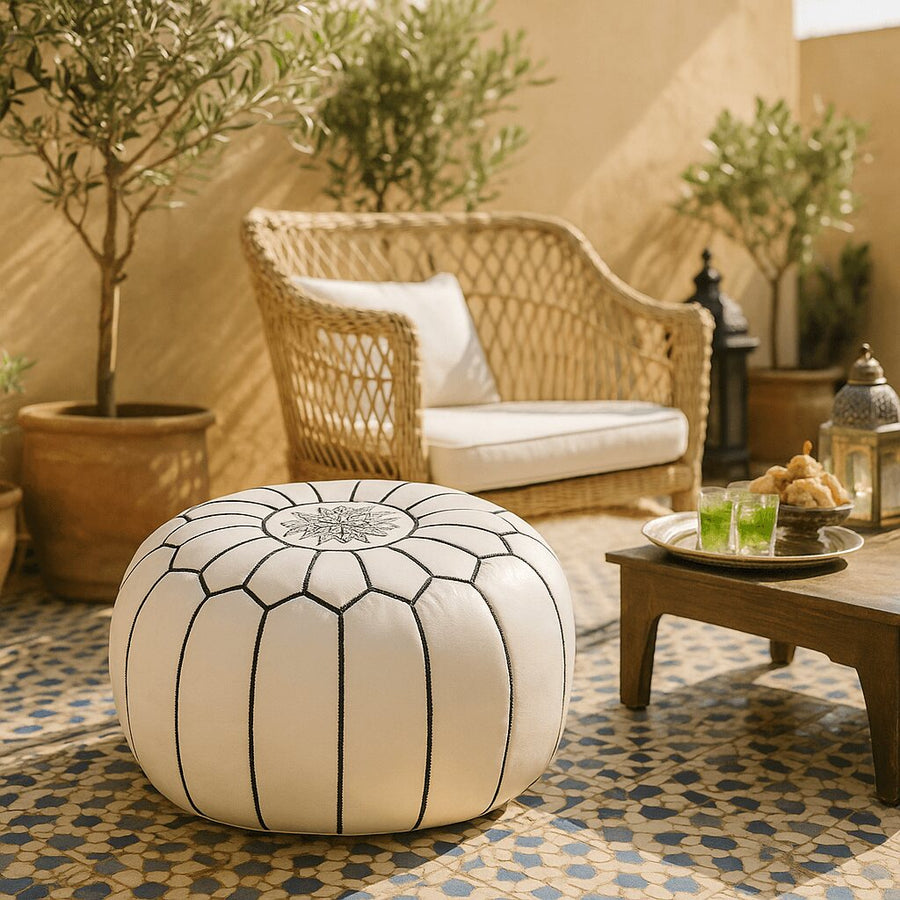 White leather pouf on a tiled Moroccan terrace with wicker furniture and potted olive trees