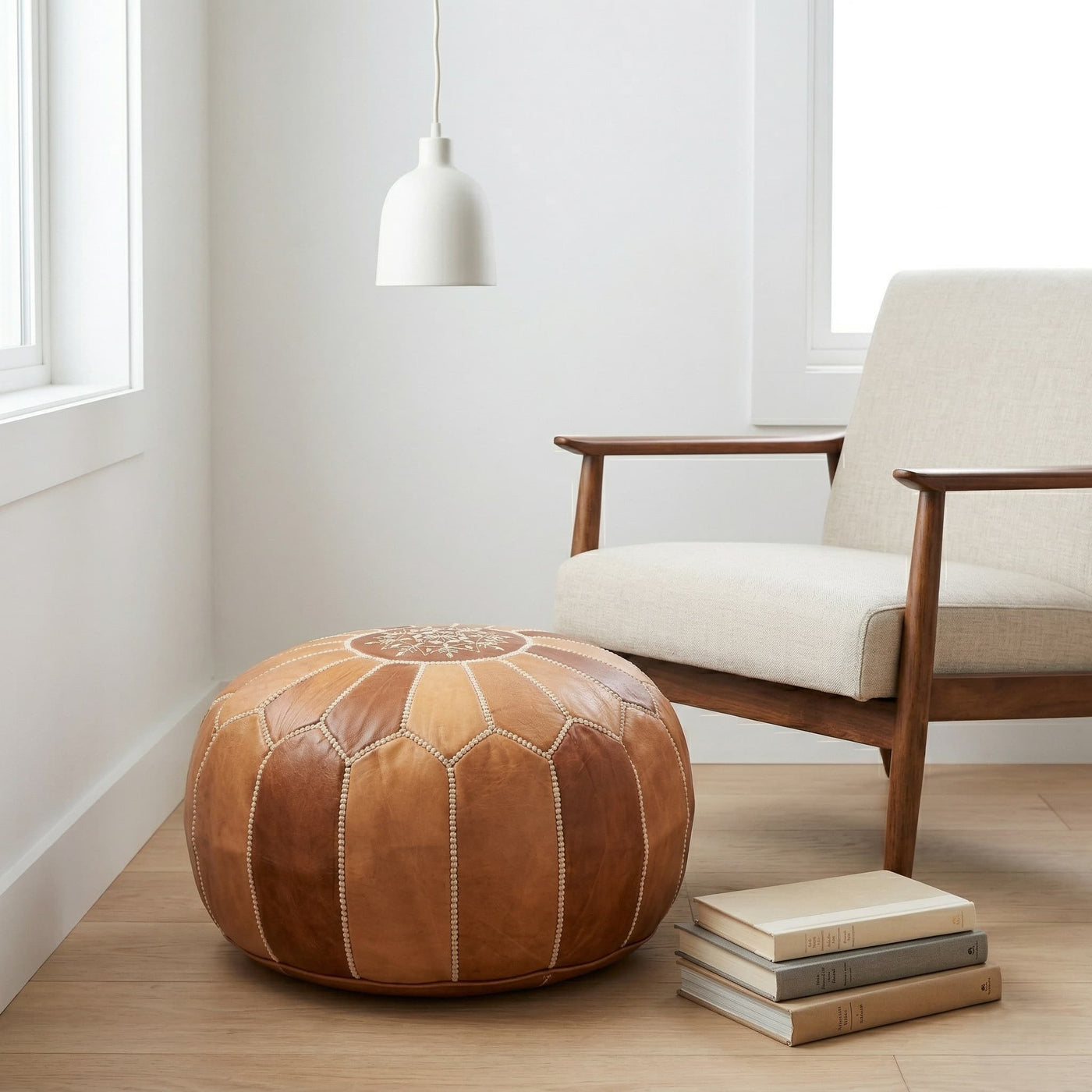 Tan leather pouf used as a footrest beside a mid-century armchair in a bright white room
