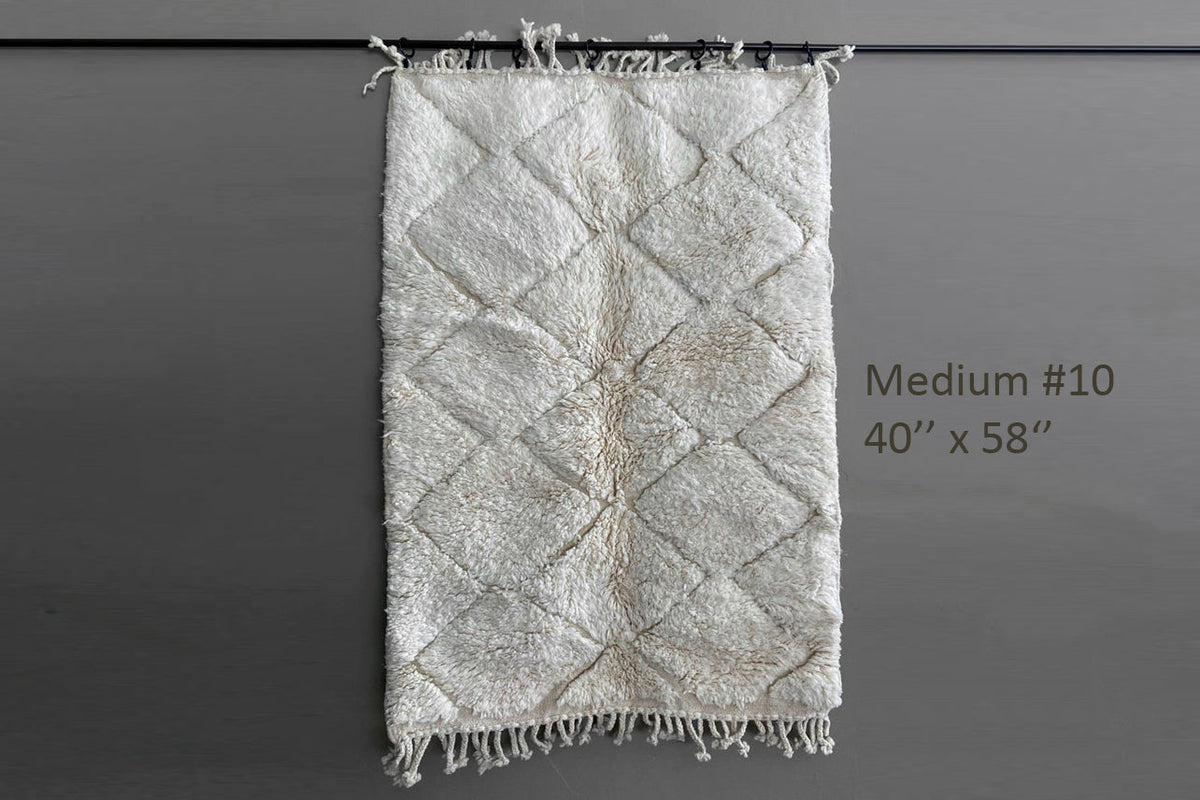 Cream and beige Berber rug with diamond pattern and fringe ends, displayed flat against gray background.