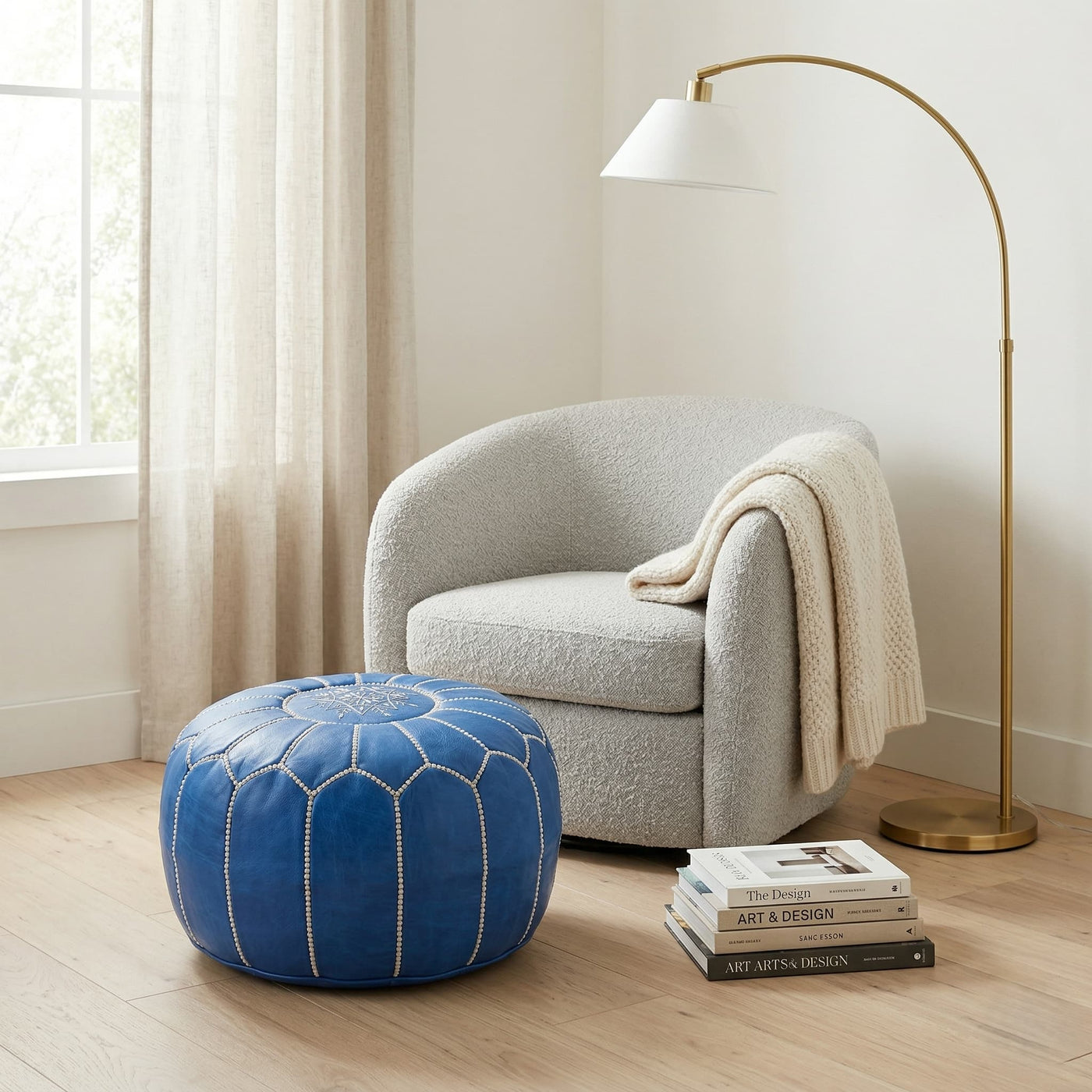 Denim blue Moroccan round pouf beside a cream boucle armchair and brass floor lamp
