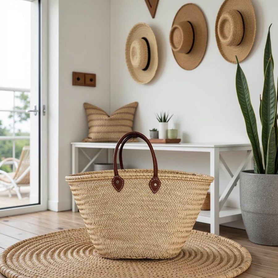Palm leaf market basket with short handheld leather handles on a round woven rug beside a hallway bench