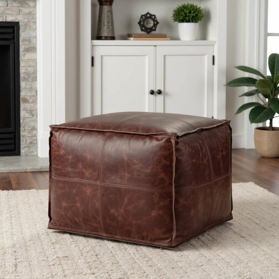 Dark brown square leather ottoman in a living room beside a white fireplace