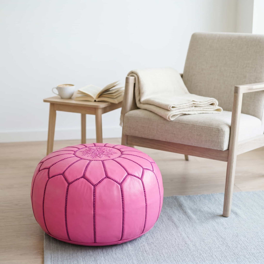 Pink leather pouf used as a footrest beside an armchair in a bright reading nook