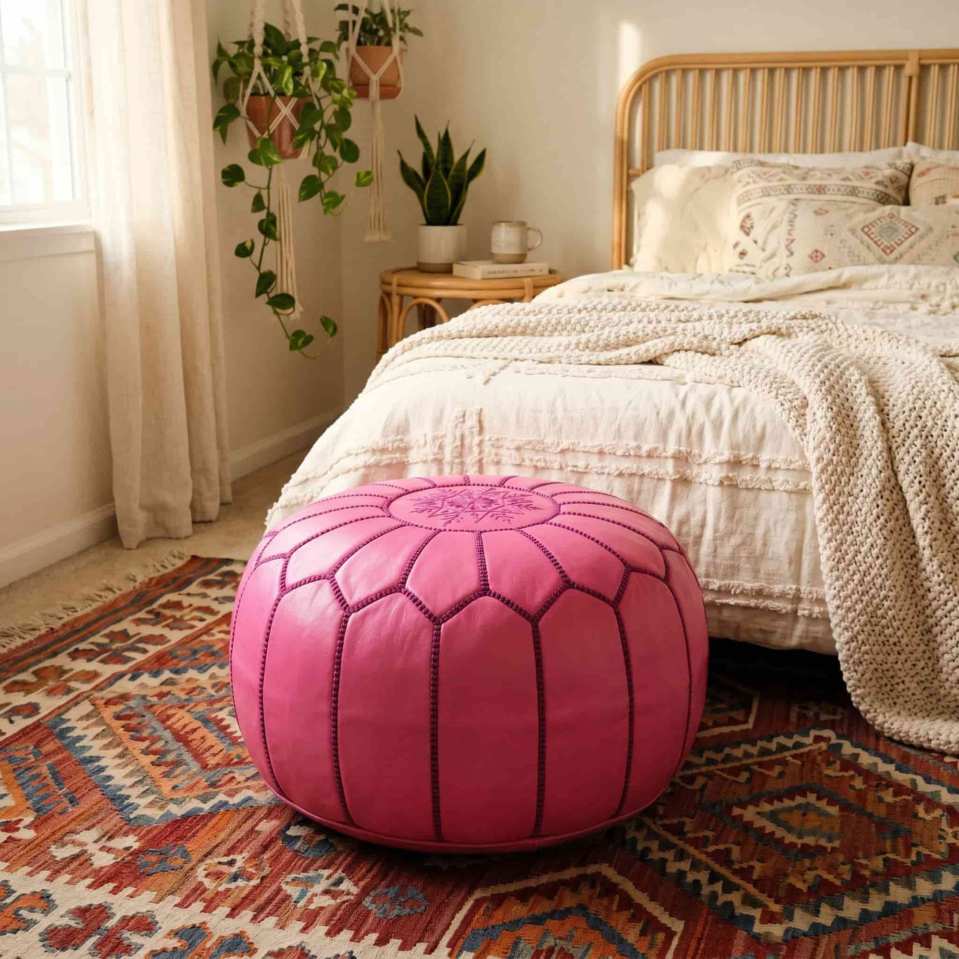 Pink leather pouf on a patterned rug in a boho bedroom with rattan headboard
