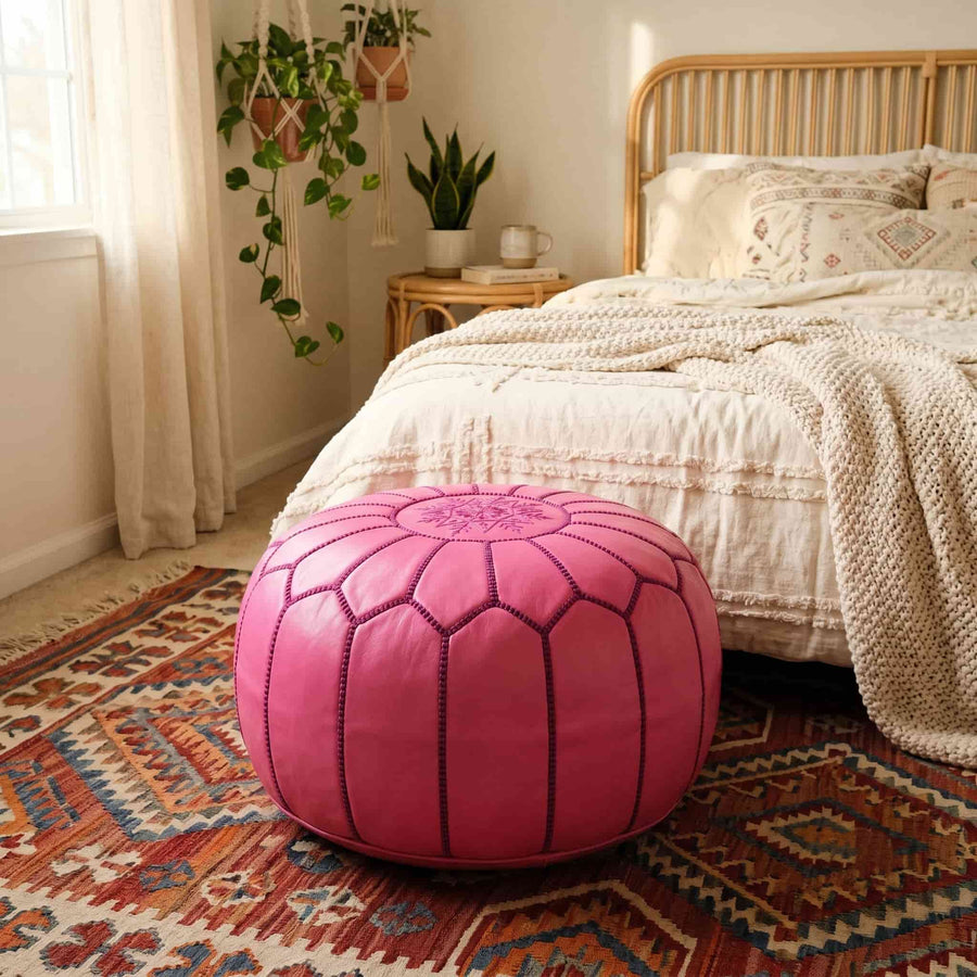 Pink leather pouf on a patterned rug in a boho bedroom with rattan headboard