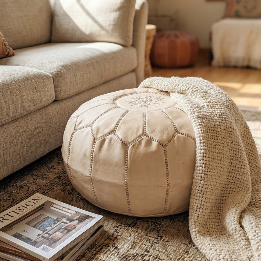 Cream undyed leather pouf beside a sofa with a draped throw