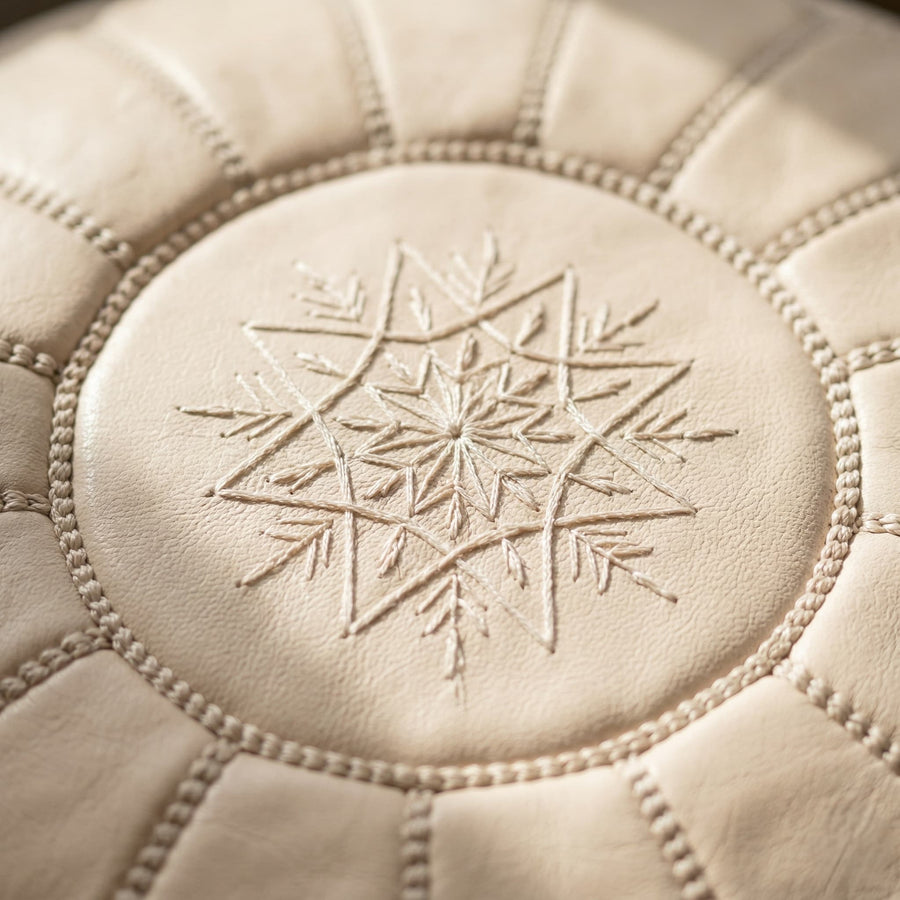 Undyed leather pouf stacked above a tan pouf against an exposed brick wall