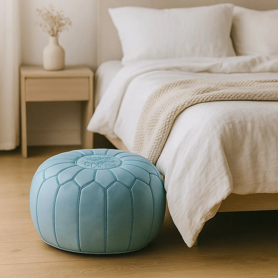 Sky blue leather pouf on an oak floor beside a minimalist wooden bed with white linen bedding