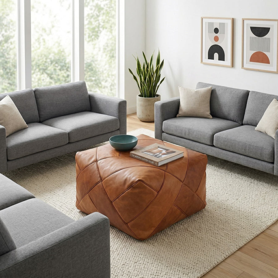 Tan square leather pouf used as a coffee table between two grey sofas on a cream wool rug