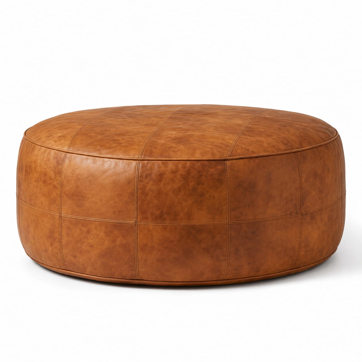 Round tan leather floor ottoman with plain hand-stitched panels, on a plain white background